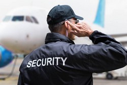 Rear view of mature security guard listening to earpiece against building by AndreyPopov via iStock.